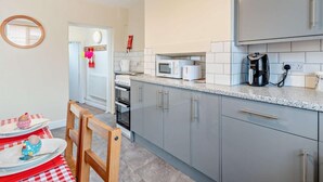 A compact kitchen with grey cabinets, a microwave, a coffee maker, and a small dining area with a red and white checkered tablecloth. - 2 Bed in Fakenham (oc-92173) (Fakenham)