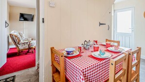 A dining area with a checkered tablecloth, wooden chairs, and a red carpet. - 2 Bed in Fakenham (oc-92173) (Fakenham)