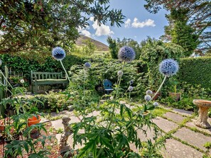 Un jardin avec un sentier en pierre, un banc en bois et différentes plantes.