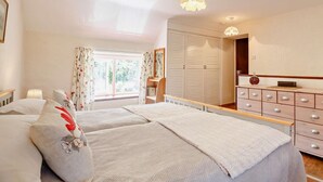 Un dormitorio con cama, mesitas de noche, armario y ventana con cortinas.