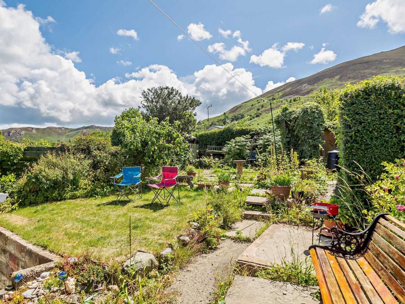 A garden with a bench, a pathway, and a hill in the background.