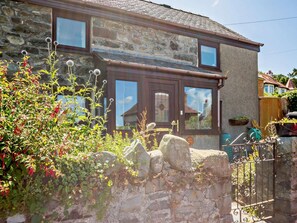 A stone house with a brown door and windows, surrounded by greenery and a stone wall. - 1 Bed in Penmaenmawr (oc-92421) (Dwygyfylchi)