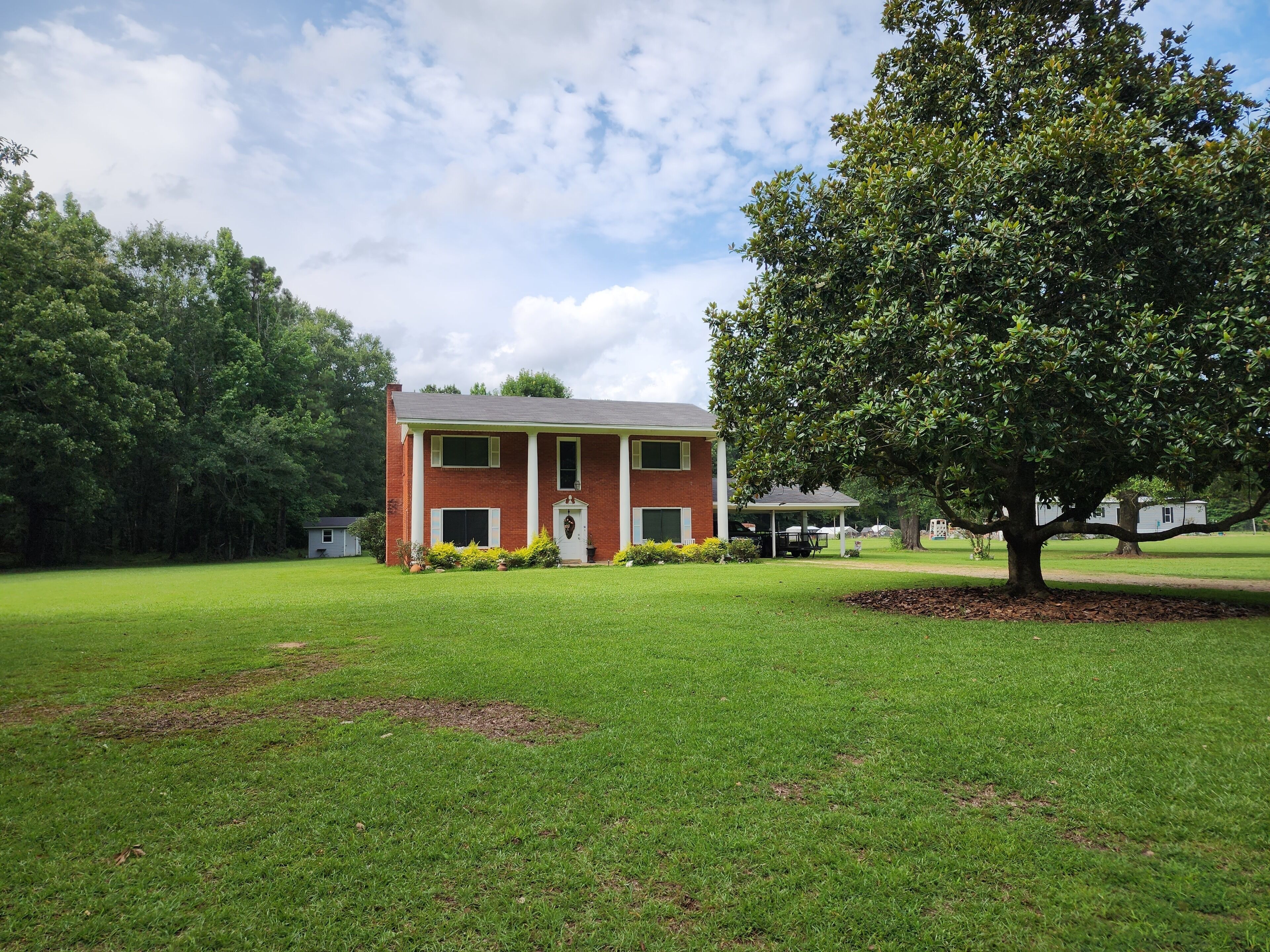 A two-story brick house with a covered porch, surrounded by a well-maintained lawn and a large tree.