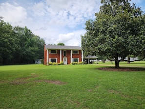 A two-story brick house with a covered porch, surrounded by a well-maintained lawn and a large tree.