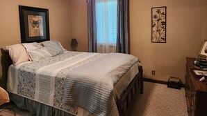 A bedroom with a bed, a ceiling fan, a window with curtains, a wall-mounted picture, and a dresser with books. - The Madison
2 story colonial style home built in 1978, with my father's own hand (Crossett)