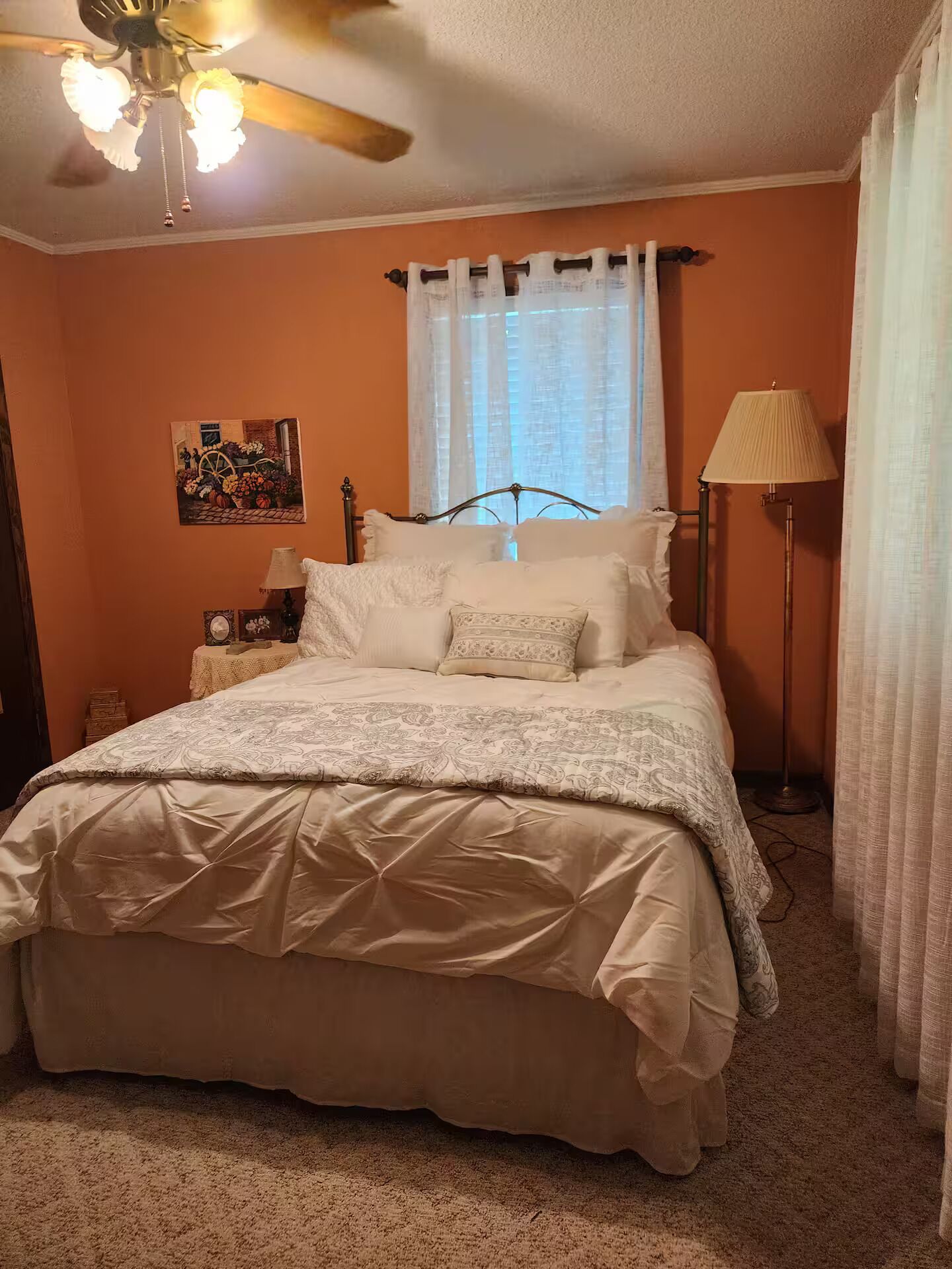 A bedroom with a bed, a nightstand, a lamp, a ceiling fan, and a window with curtains.