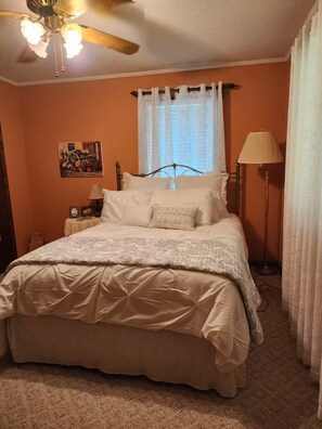 A bedroom with a bed, a nightstand, a lamp, a ceiling fan, and a window with curtains.
