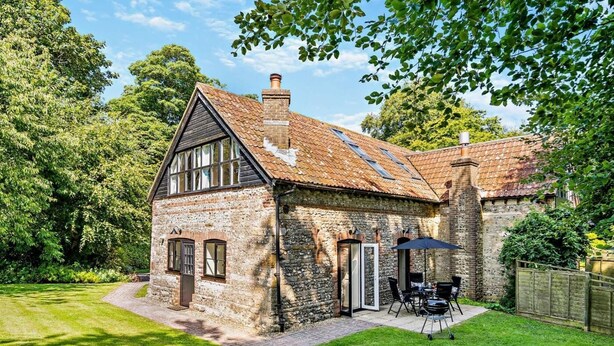 A stone house with a sloped roof, a chimney, and a small patio with outdoor furniture. - 2 Bed in Dorchester (oc-92416) (West Dorset District)