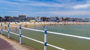 A coastal promenade with a beach, promenade railing, and buildings in the background. - 2 Bed in Dorchester (oc-92416) (West Dorset District)