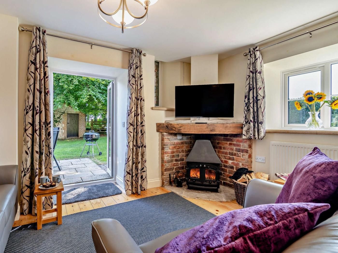A cozy living room with a fireplace, a television, and a view of the garden.