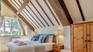 A bedroom with a sloped ceiling, a bed with white linens, blue patterned pillows, a wooden nightstand, a wooden wardrobe, and a window with curtains. - 2 Bed in Dorchester (oc-92416) (West Dorset District)