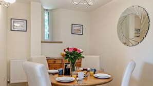 A dining area with a round table, white chairs, a vase with flowers, and a wall-mounted mirror. - 2 Bed in Dorchester (oc-92416) (West Dorset District)