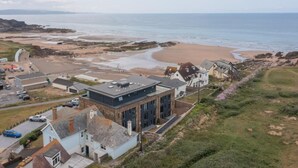 Un bâtiment situé sur la côte, doté d’un toit plat, et jouxtant une plage de sable avec des affleurements rocheux.