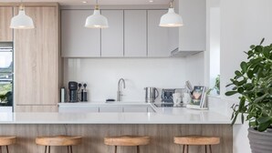 Une cuisine moderne dotée d’un îlot central, de tabourets de bar, de luminaires suspendus et offrant une vue sur un paysage.