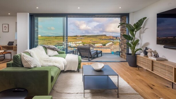 Un salon moderne avec un canapé vert, une table basse et une vue sur un paysage grâce à de grandes fenêtres.