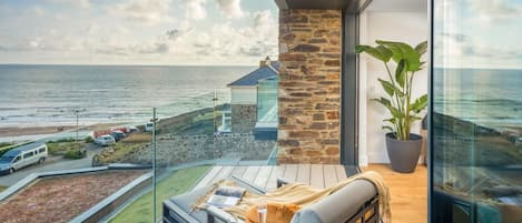 A balcony with a view of the sea, a stone wall, and a potted plant.