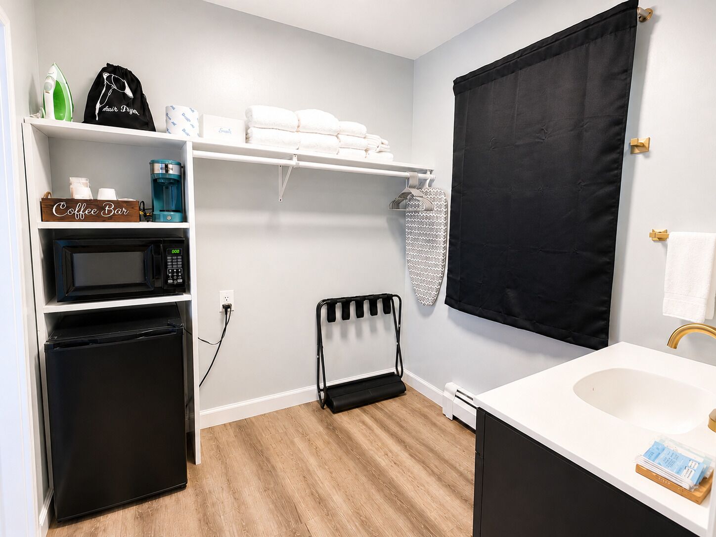 A compact bathroom with a white sink, a black towel rack, a microwave, a coffee bar, and a black radiator.