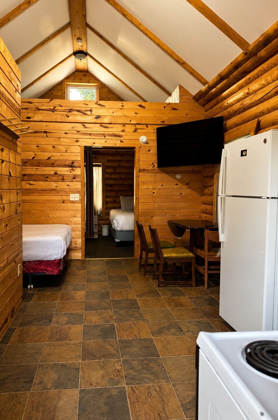 A log cabin interior with a kitchen, a dining area, a bed, and a bathroom.