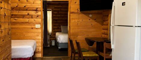 A log cabin interior with a kitchen, a dining area, a bed, and a bathroom.