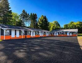 Filas de cabañas tipo motel con entradas individuales, un estacionamiento de grava y un fondo de árboles.