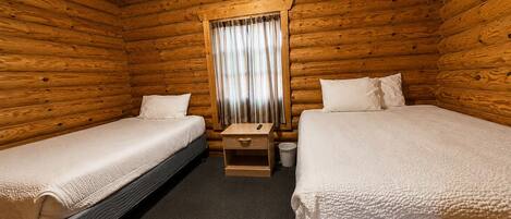 A cabin room with two beds, a small wooden nightstand, a window with curtains, and a carpeted floor.