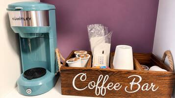 Una cafetera, sobres de azúcar, una taza de café y una caja de madera con la etiqueta 'Coffee Bar' en un estante.
