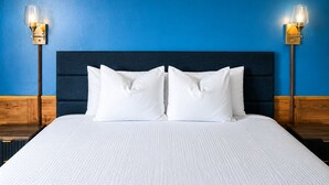 A bed with white bedding, a dark headboard, and two wall-mounted lamps. - Blisspoint Munising (Munising)