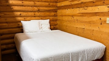 Een eenpersoonsbed met een witte matras en rode beddengoed in een kamer met houten wanden.