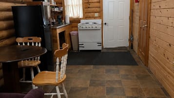 Et interiør af en hytte med spiseplads, køkken og en dør, der fører til et andet rum.