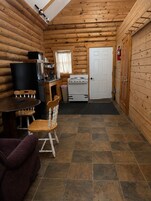 Interior de una cabaña de troncos con comedor, cocina y una puerta que da a otra habitación.