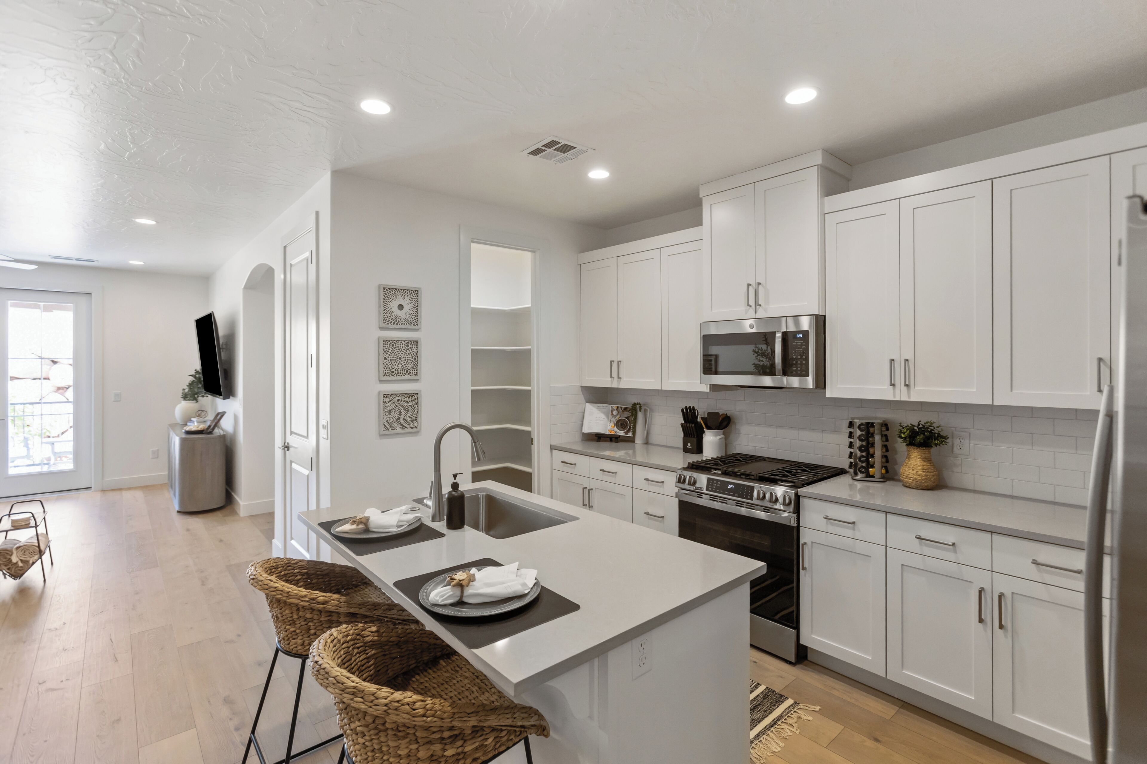 A modern kitchen with white cabinetry, a central island, stainless steel appliances, and a dining area with wicker chairs.
