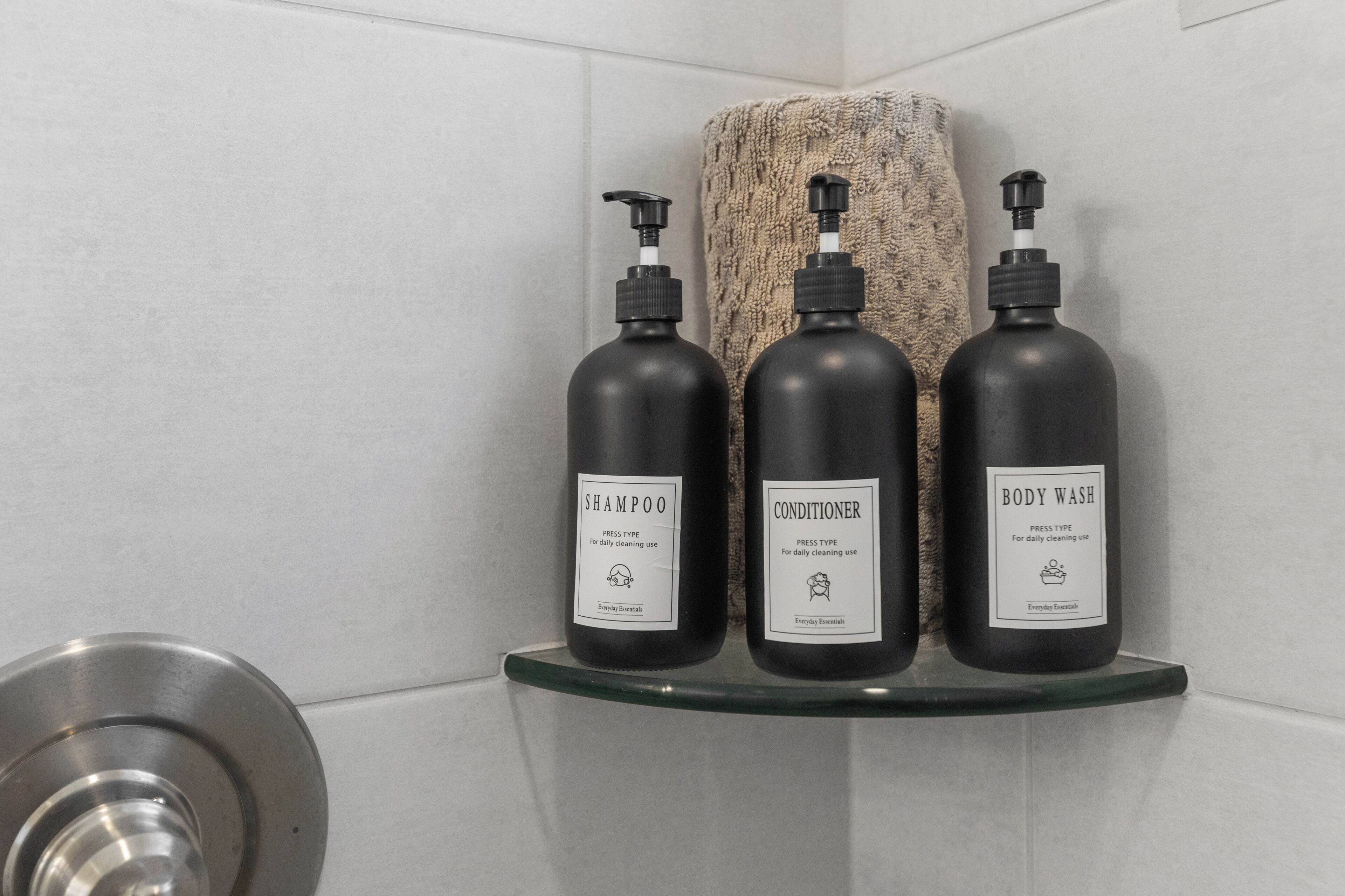 Drie flessen toiletartikelen op een glazen plank in een badkamer.