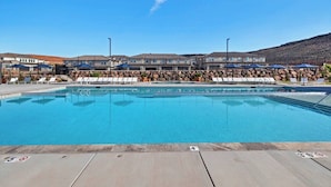 Une piscine entourée de bâtiments dotés d’un mur en pierre, avec des chaises longues et des parasols à proximité.