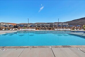 Une piscine entourée de bâtiments dotés d’un mur en pierre, avec des chaises longues et des parasols à proximité.