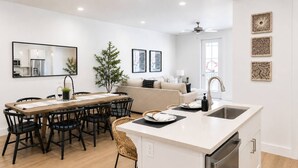 Une cuisine moderne avec un coin repas, des meubles blancs et un îlot central doté d’un évier.