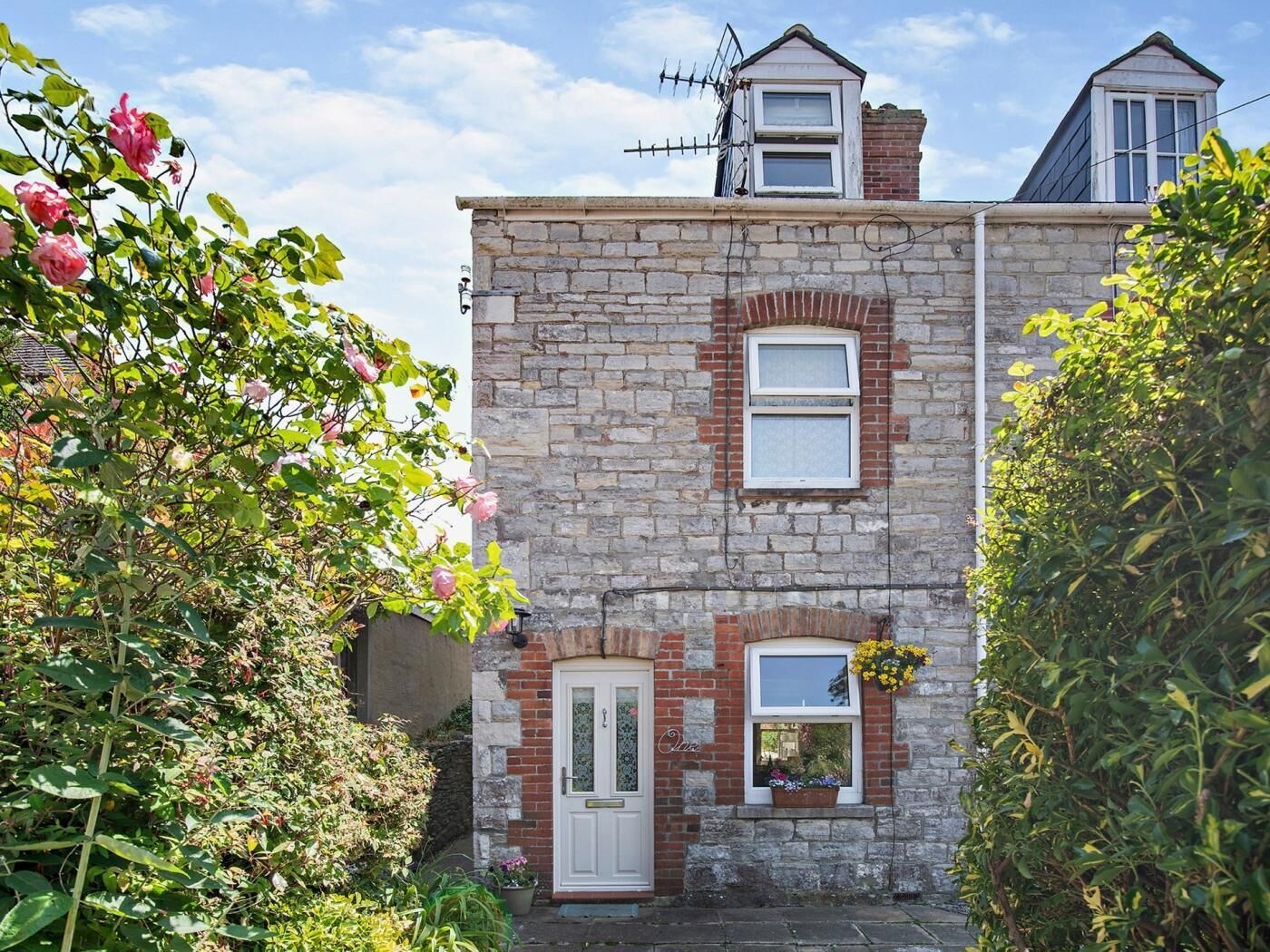 A two-story stone building with a white door, a small window with a flower box, and a chimney.