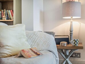 Ein ordentlich bezogenes Bett mit einem weißen Kopfkissen und einem Buch, ein Nachttisch mit einer Lampe, einer Tasse und einem dekorativen Gegenstand.
