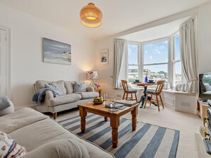 Ein Wohnzimmer mit einer Couch, einem Couchtisch, einem Fernseher und einem Essbereich mit Stühlen und einem Tisch.