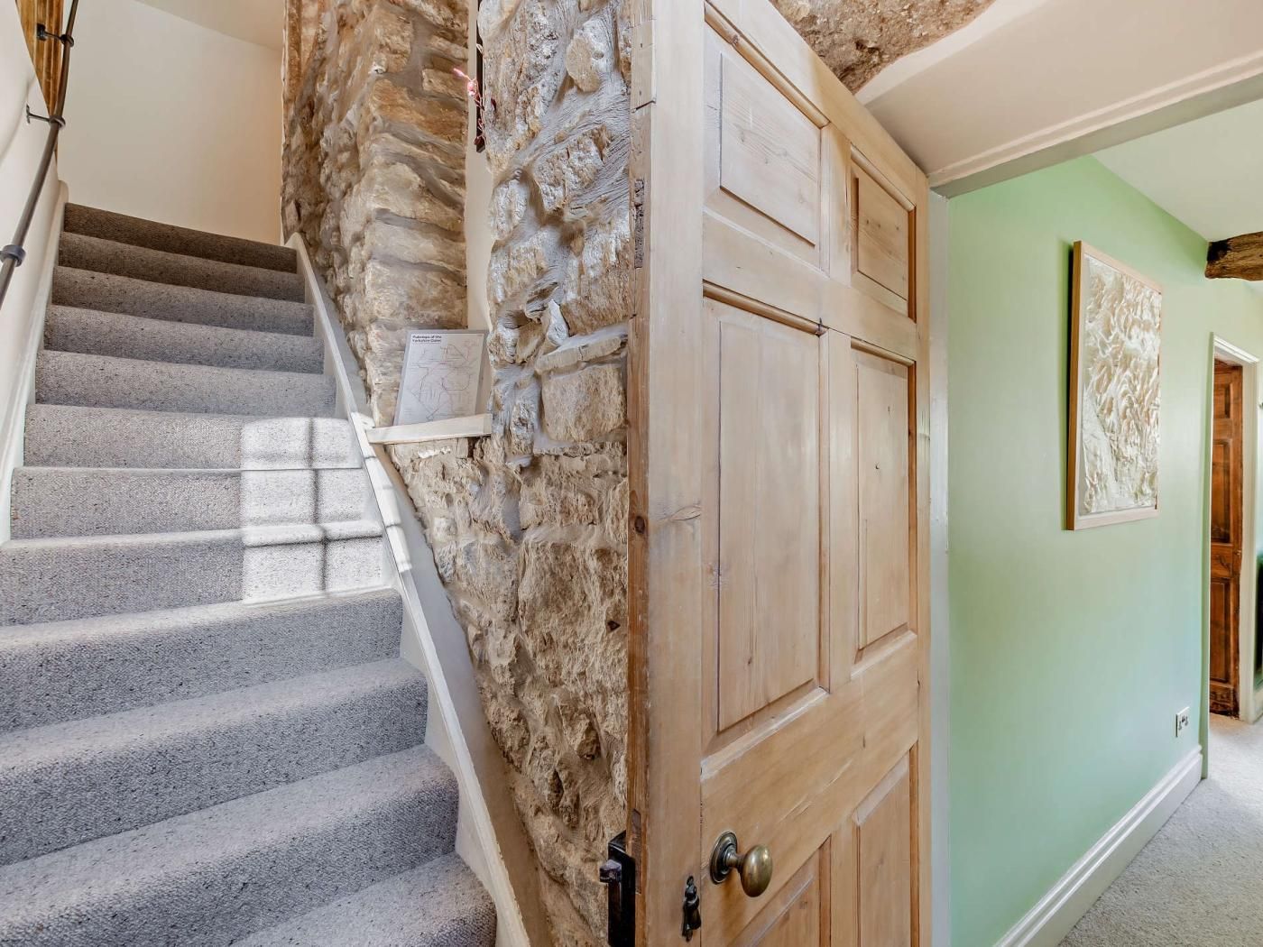 A staircase with stone walls, a wooden door, and a green wall with a framed picture.