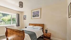 Une chambre à coucher avec un lit en bois, une table de chevet, un tableau encadré et une fenêtre avec des rideaux.