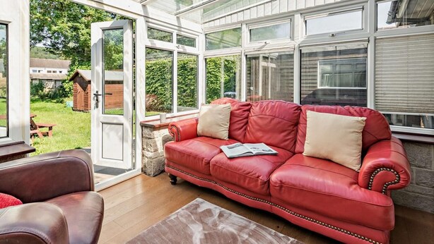 Une véranda avec un canapé en cuir rouge, une table en bois et une vue sur un jardin.