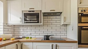 Une cuisine avec des meubles blancs, un four à micro-ondes, une cuisinière et une planche à découper avec des fruits.
