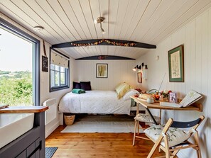 Ein gemütliches Schlafzimmer mit Bett, Schreibtisch und Stuhl, ein Fenster mit Blick und eine Decke mit dekorativem Balken.