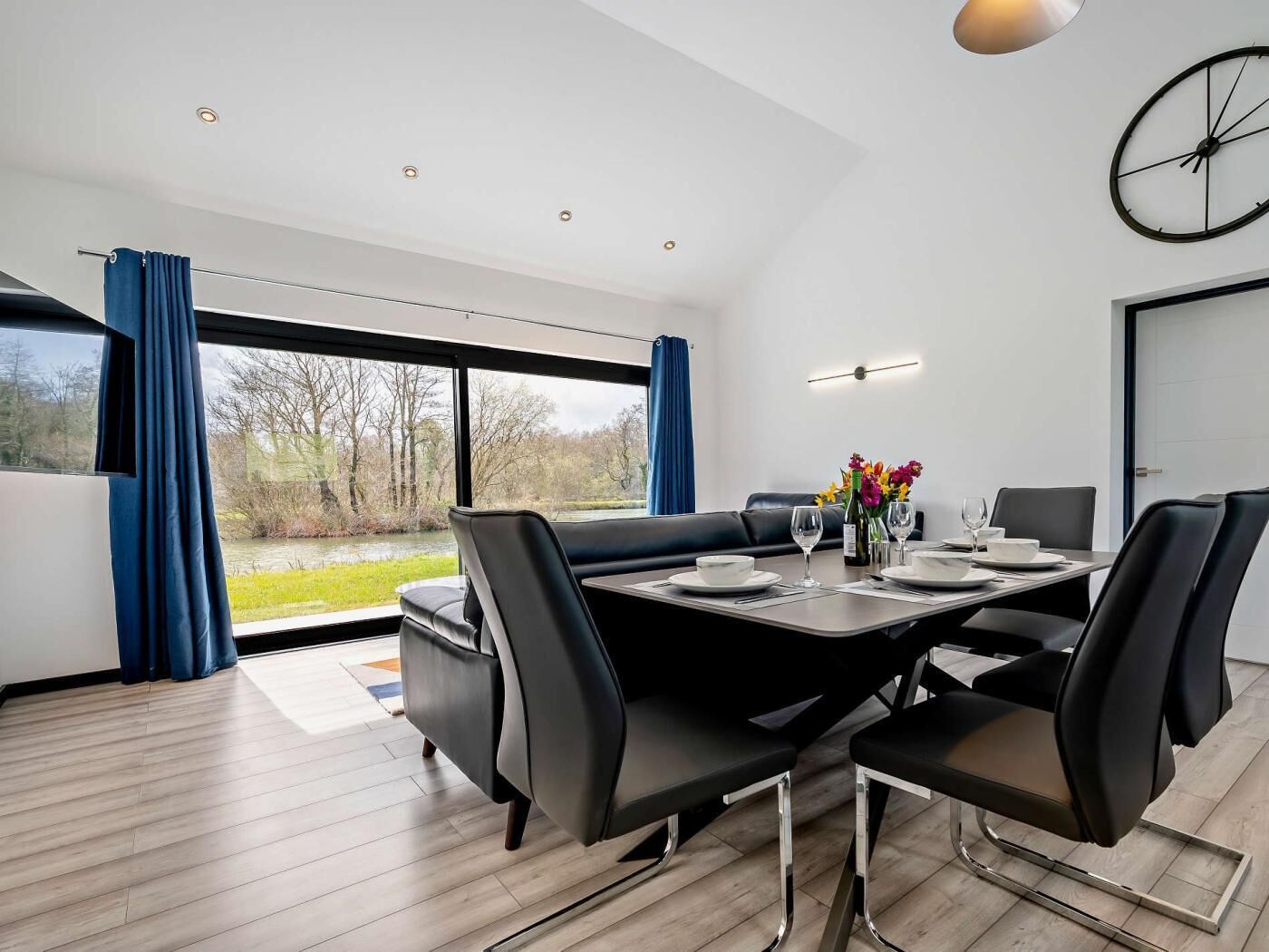 Une salle à manger moderne avec une grande table, des chaises noires et une vue sur une rivière.