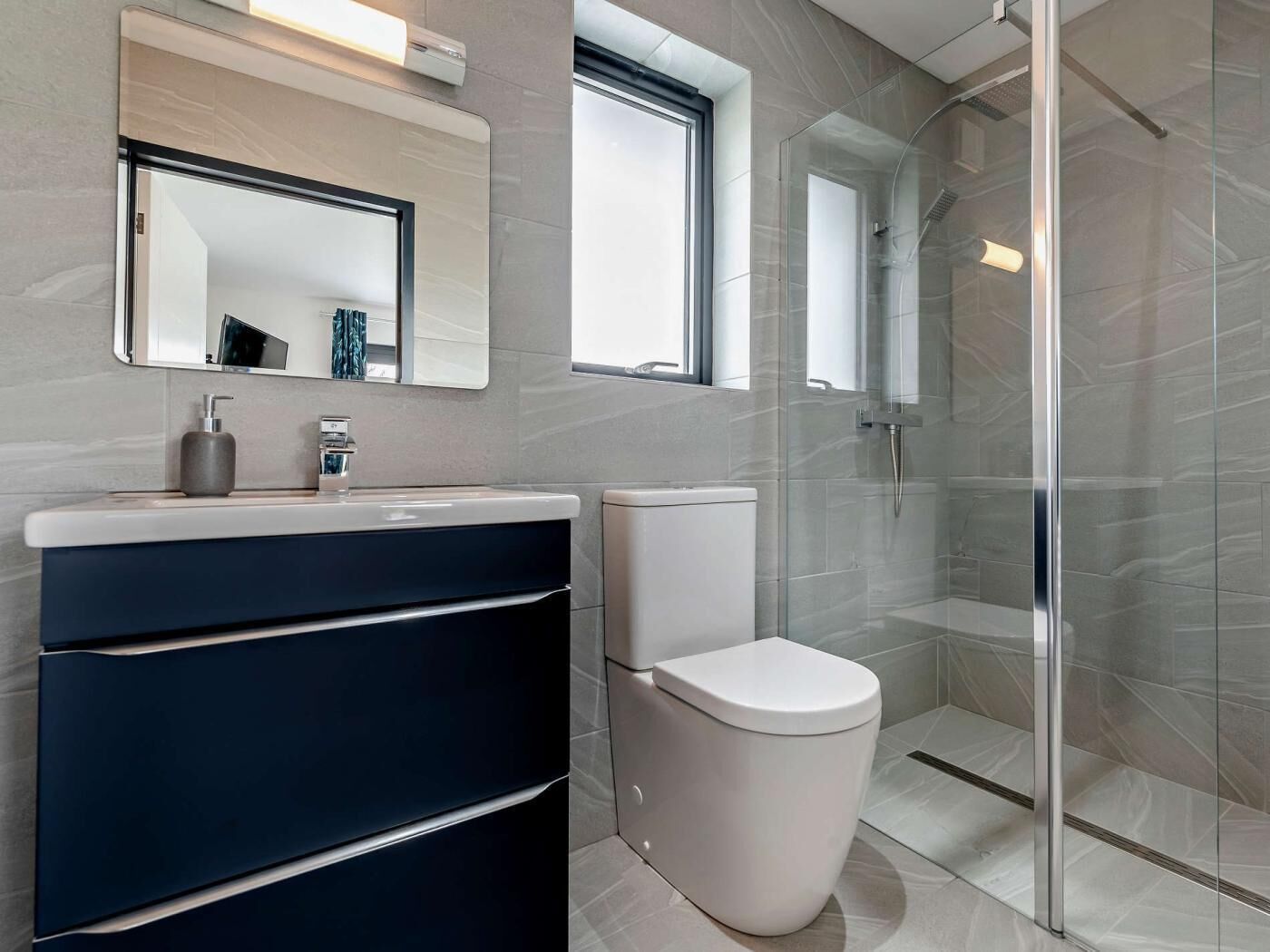 A modern bathroom with a glass shower enclosure, a white toilet, and a vanity with a mirror.