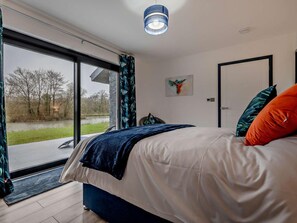 Ein Schlafzimmer mit großem Fenster, einem Bett mit weißer Bettwäsche, einem blauen Kopfteil und einem Bild an der Wand.
