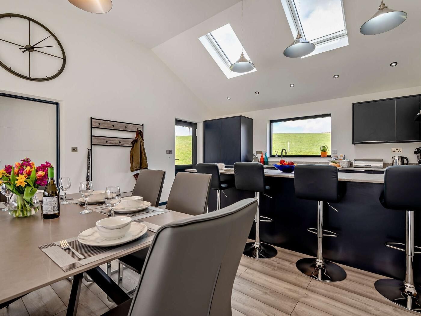 A modern kitchen with a dining area, featuring a large window, a clock, and a bar area.