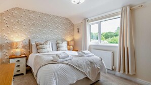 Ein Schlafzimmer mit einem Bett, Nachttischen, einem Fenster mit Vorhängen und einer Wand mit einem Blumenmuster.
