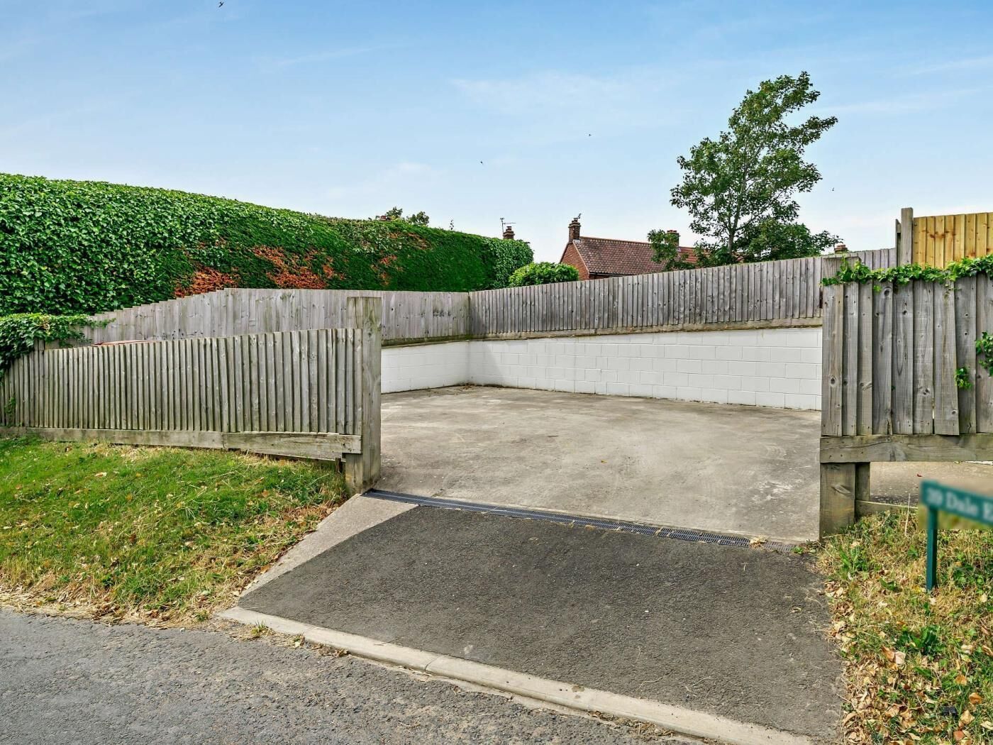 En lukket parkeringsplads med betonunderlag, omgivet af et træhegn og en hvid mur.
