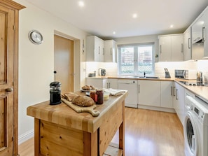 A modern kitchen with wooden cabinets, a built-in oven, a washing machine, and a window providing natural light. - 2 Bed in Hayle (oc-92505) (Gwinear)